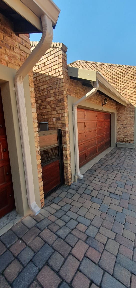 White downpipe running down the corner of a face brick home above paving